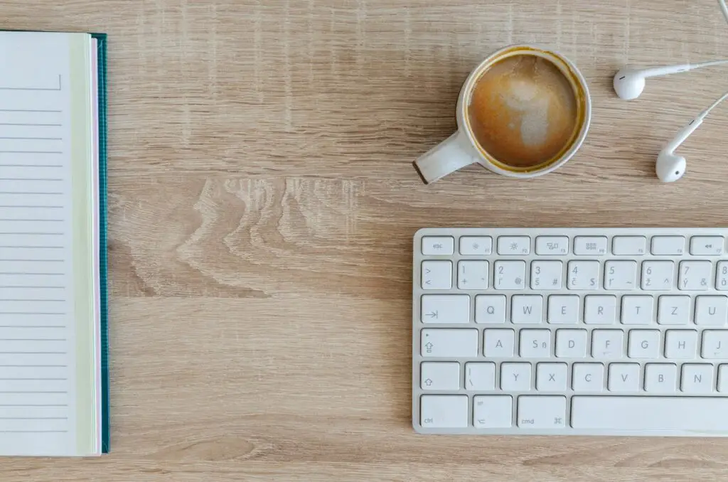 Keyboard next to a cup of coffee and headphones